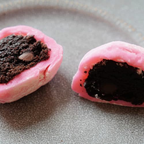 A pink mochi cut in half to reveal a chocolate brownie in the center.