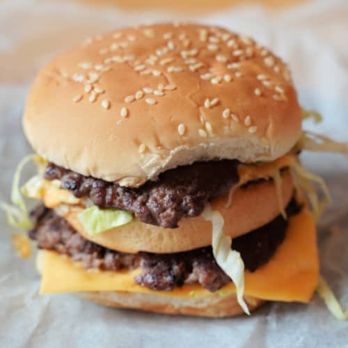 A burger with a sesame seed bun and two burger patties, cheese, and lettuce.