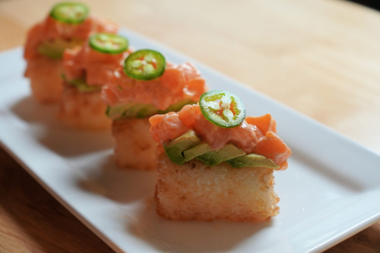 Four crispy salmon sushi on lined up on a plate.