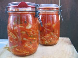 2 large canning jars on cutting board filled with kimchi.