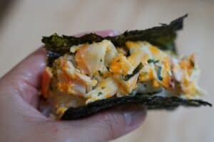 Fingers holding prepared sushi baked wrapped in nori sheet.