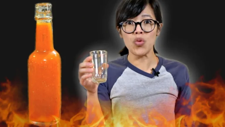 Emmy holding empty glass with flames surrounding her. Not sauce bottle fills frame to her right.